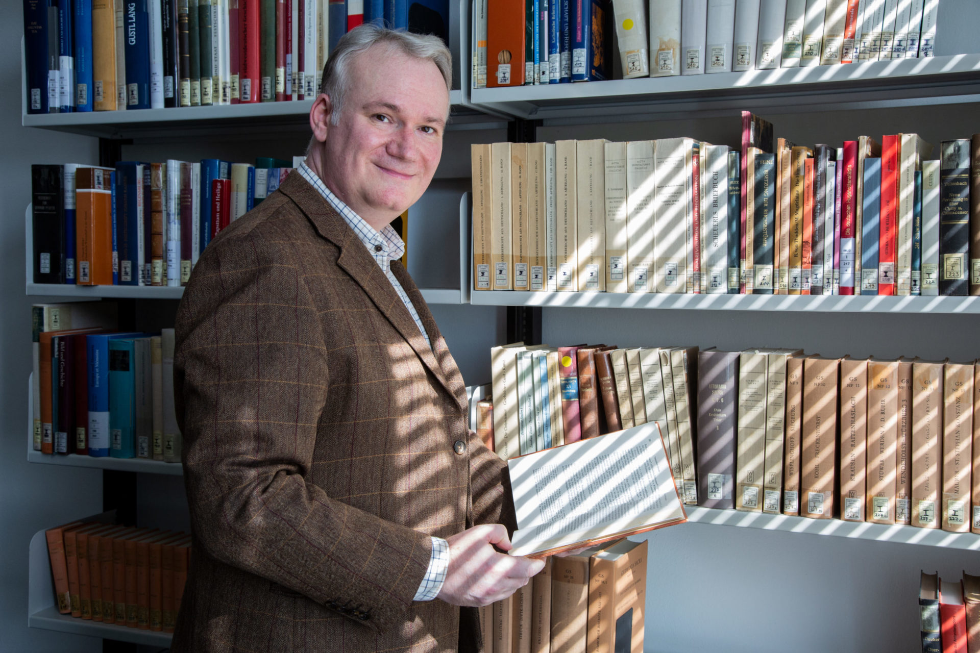 Mann steht mit einem Buch vor einem Bücherregal.