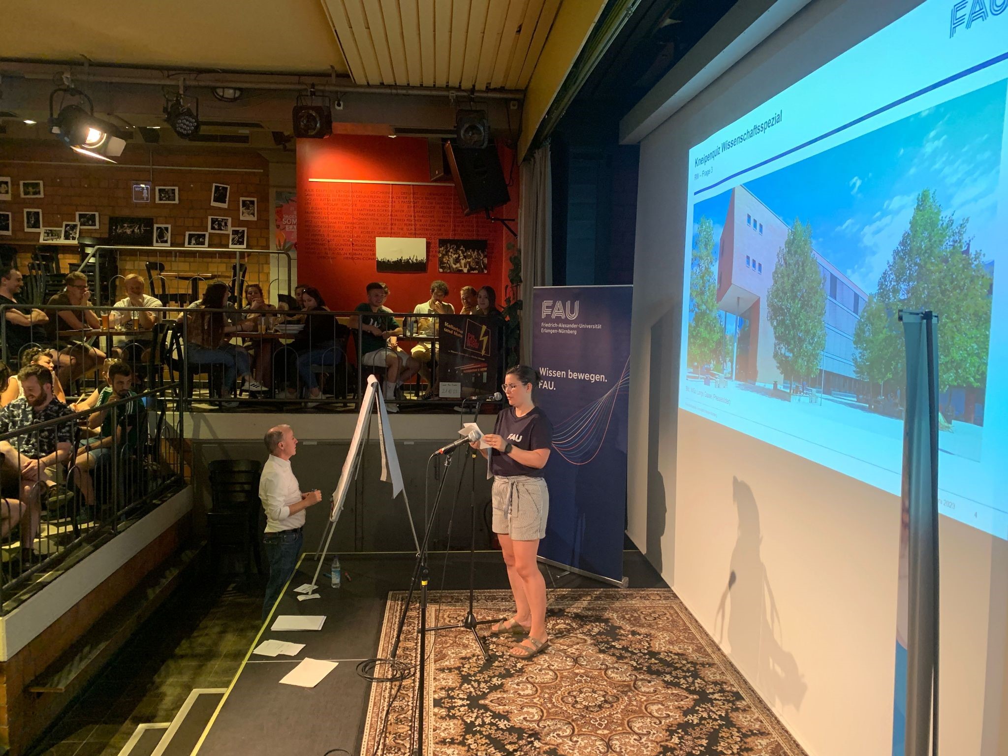 FAU-Kneipenquiz in der Kellerbühne im E-Werk: Bühne mit Moderation, Tische mit Teilnehmenden