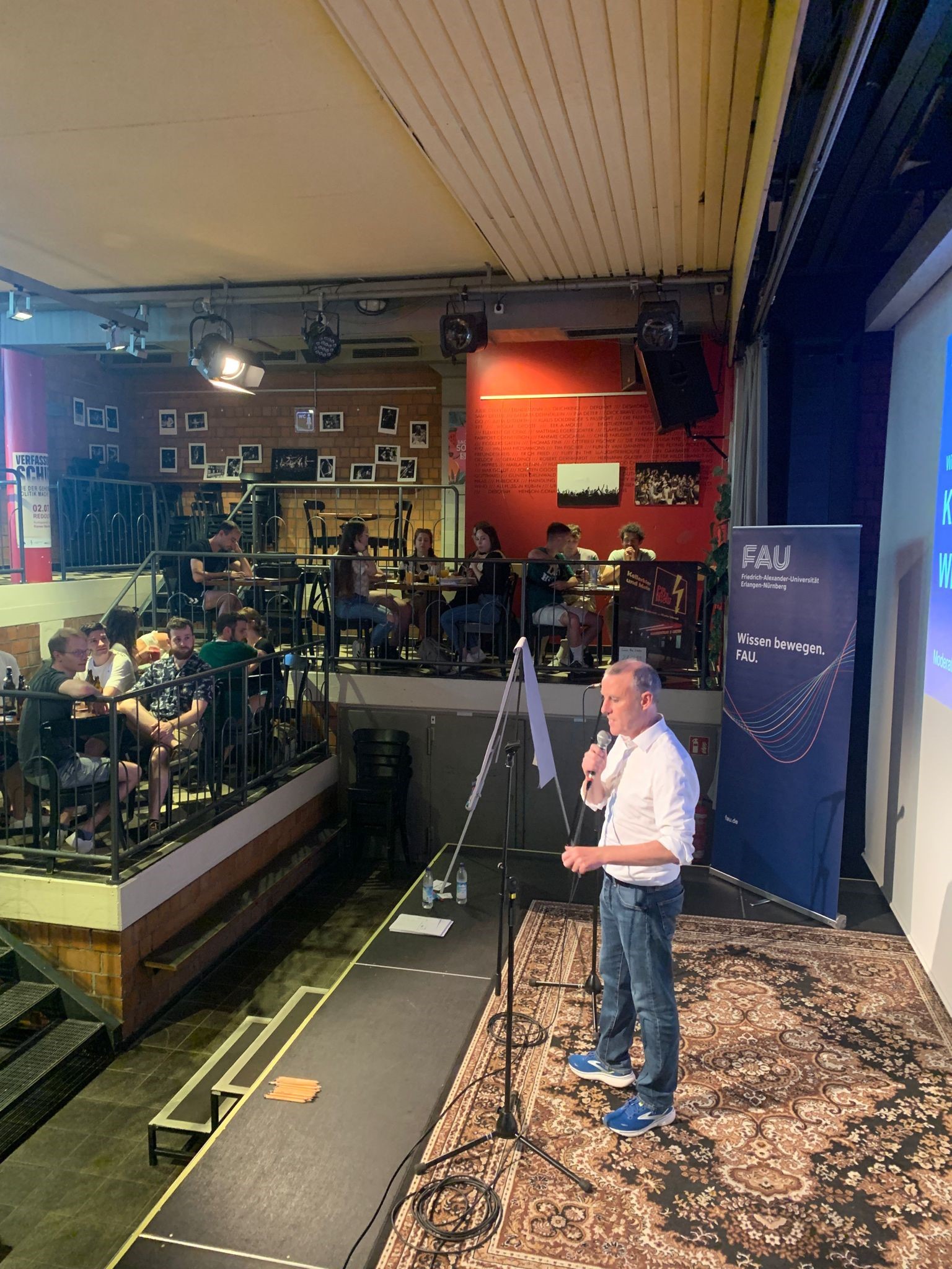 FAU-Kneipenquiz in der Kellerbühne im E-Werk: Bühne mit Moderation, Tische mit Teilnehmenden