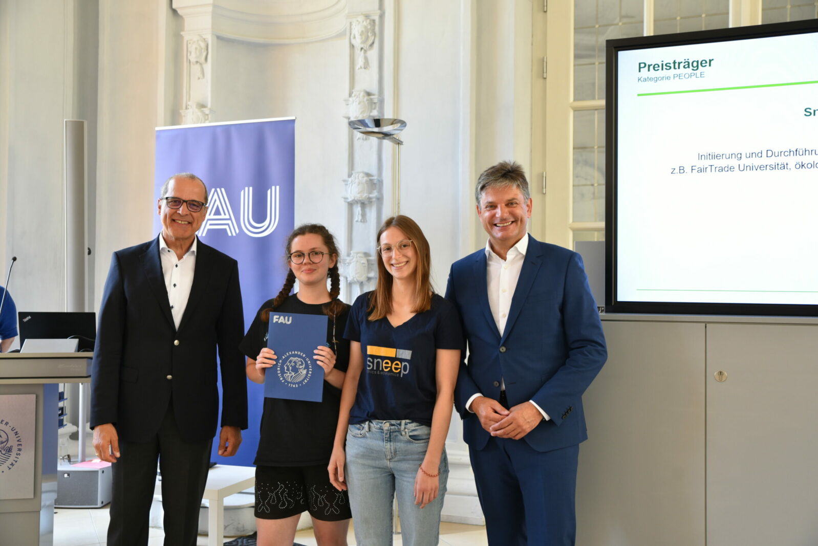 Zwei Studentinnen von Sneep mit dem FAU-Präsidenten und einem weiteren Mann im Anzug.