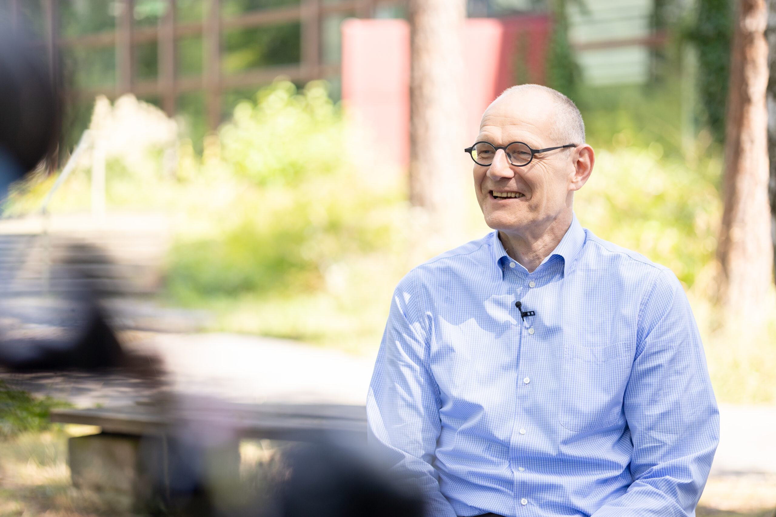 Dr. Bernd Montag an der Naturwissenschaftlichen Fakultät der FAU, auf einem Stuhl sitzend im Grünen vor dem Physikum.