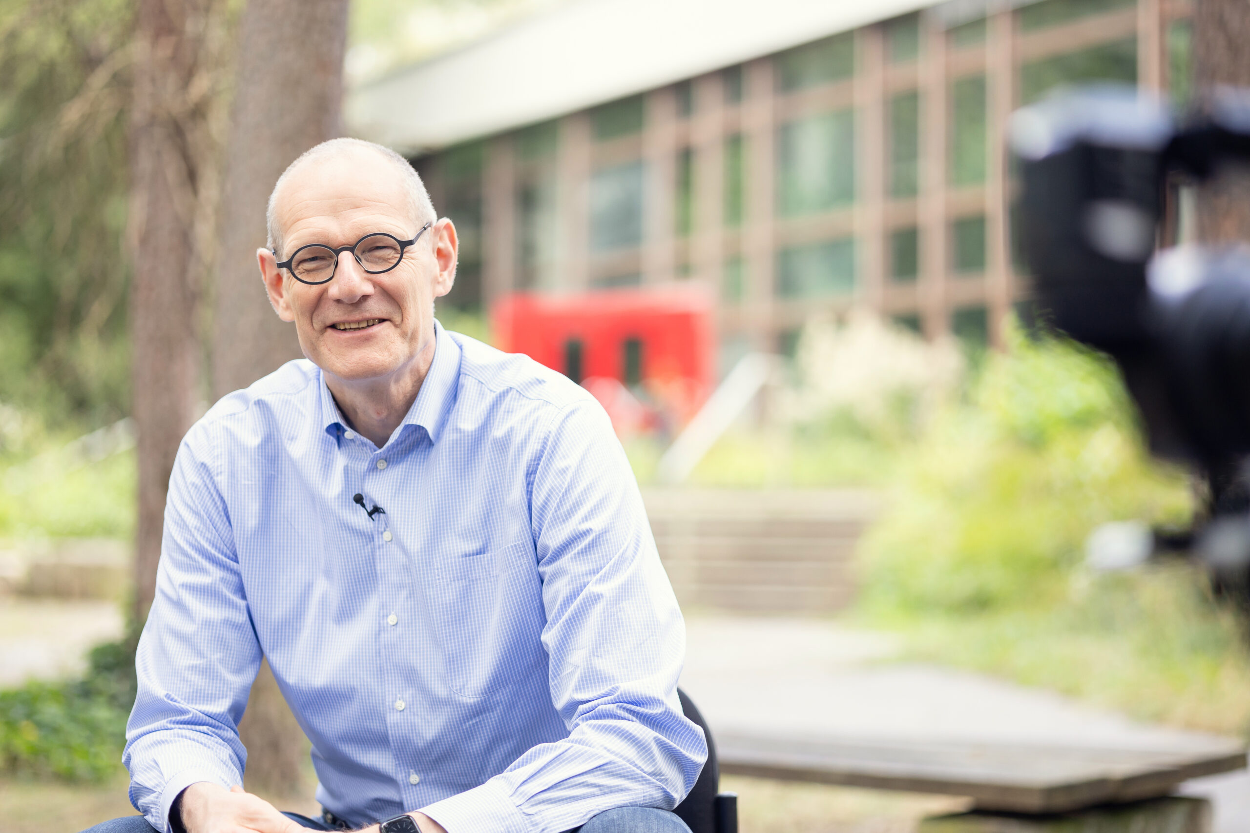 Dr. Bernd Montag an der Naturwissenschaftlichen Fakultät der FAU, auf einem Stuhl sitzend im Grünen vor dem Physikum.