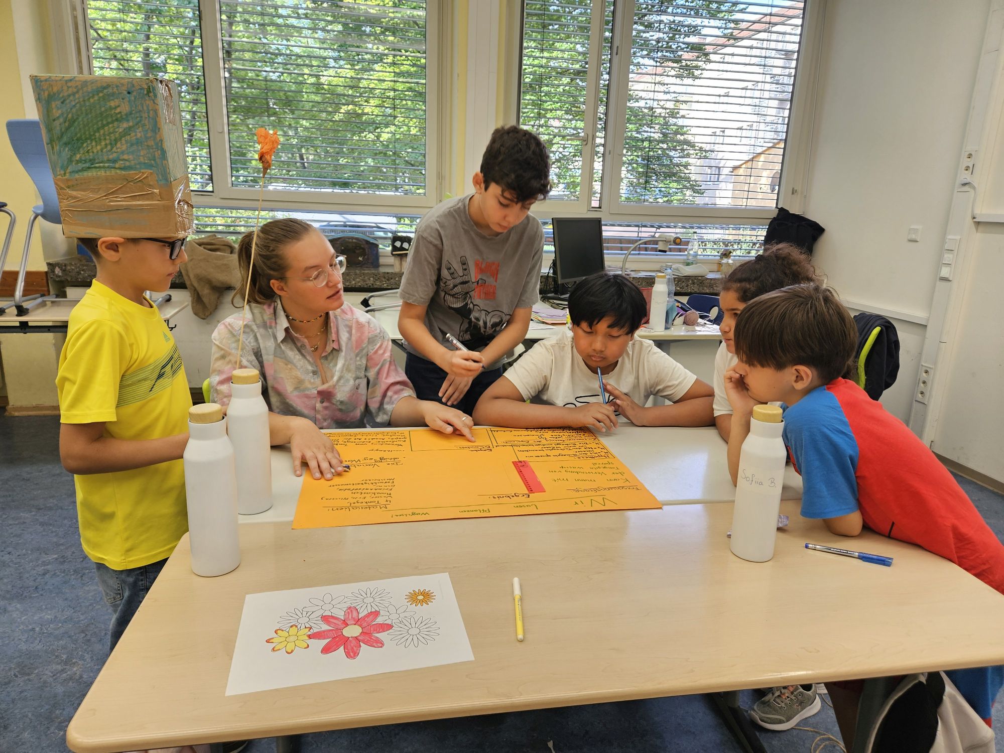 Studentin mit Kindern beim Sommercamp gemeinsam an einem Tisch