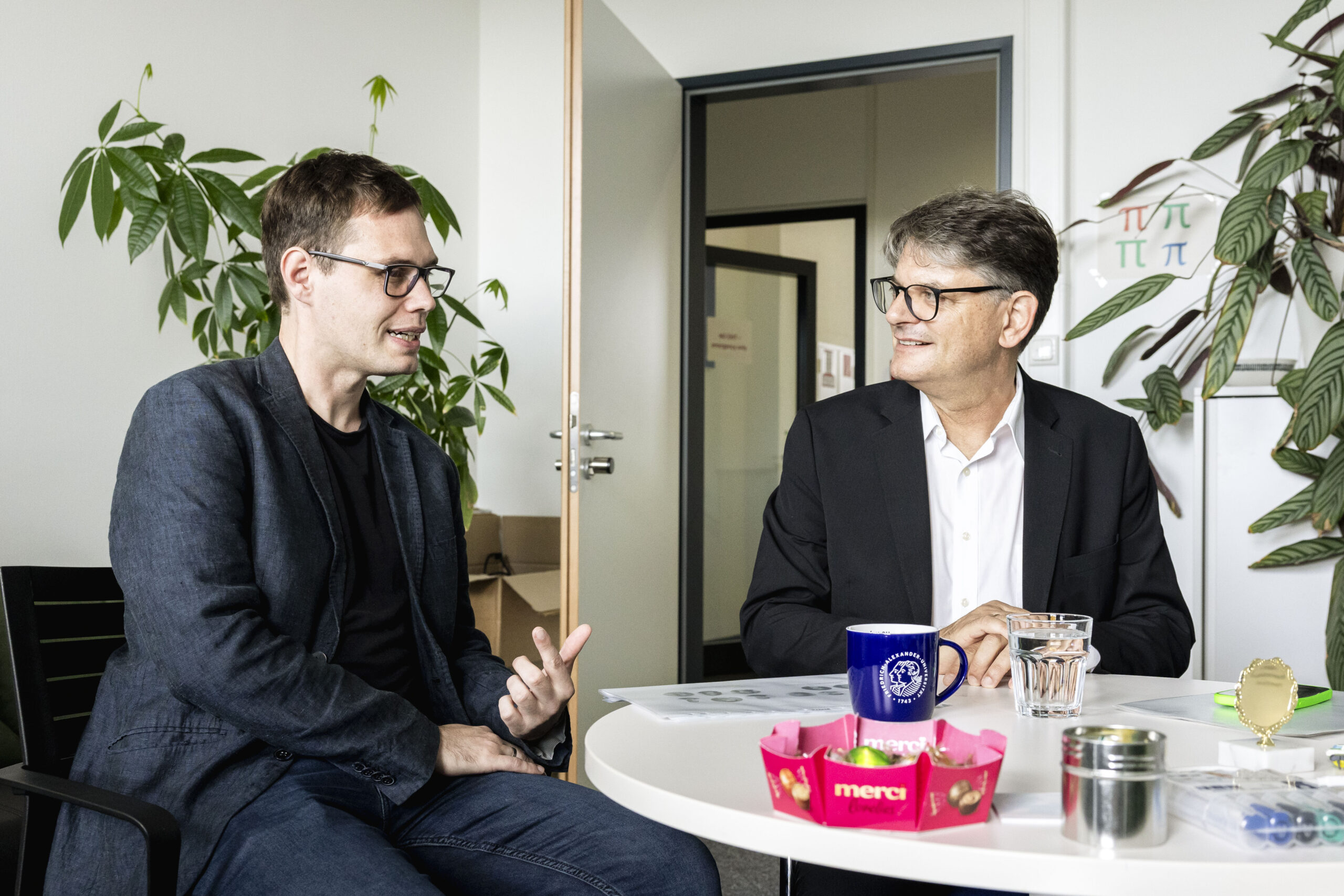 Andreas Kist und FAU-Präsident sitzen gemeinsam an einem Tisch und unterhalten sich.
