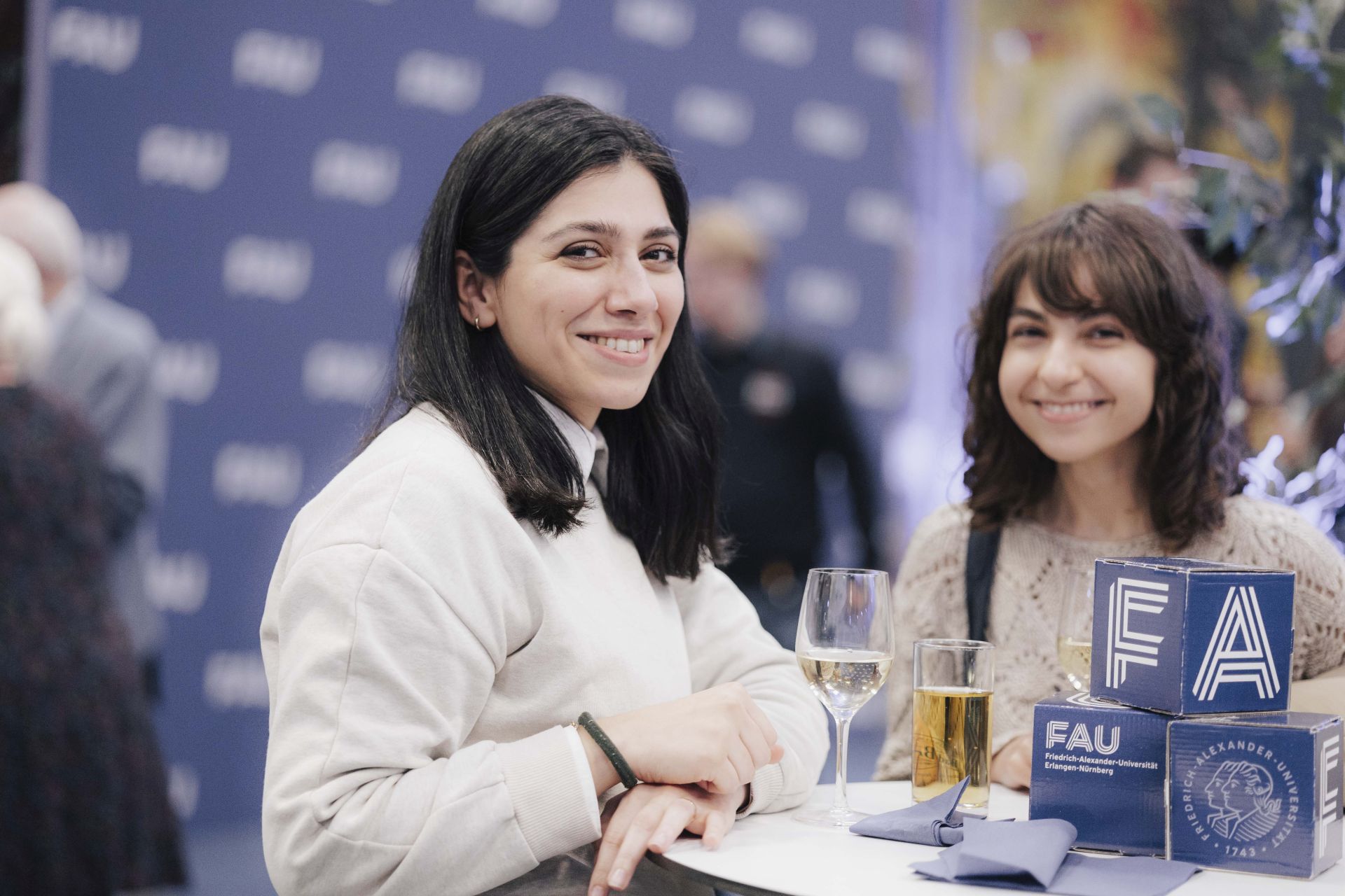 Zwei Frauen an einem Stehtisch lachen in die Kamera.