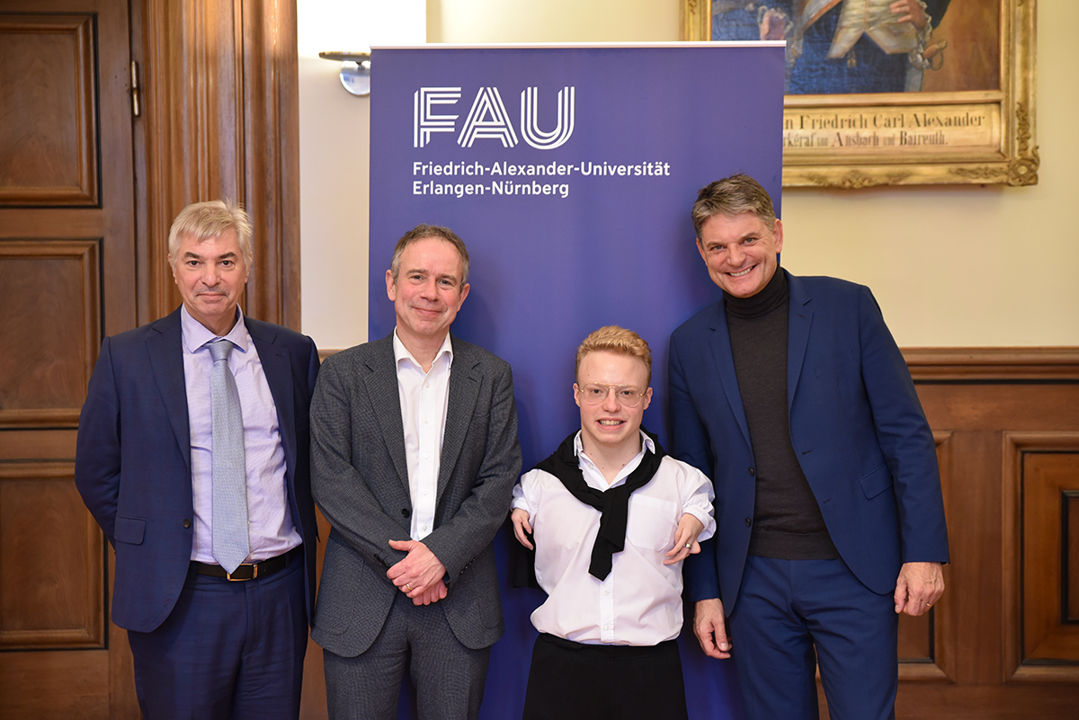 Josia Topf, FAU-Präsident Joachim Hornegger, Dekan der Rechts- und Wirtschaftswissenschaftl. Fakultät Prof. Dr. Michael Fischer und Prof. Dr. Markus Krajewski stehen zusammen gemeinsam vor blauem FAU-Roll-up.