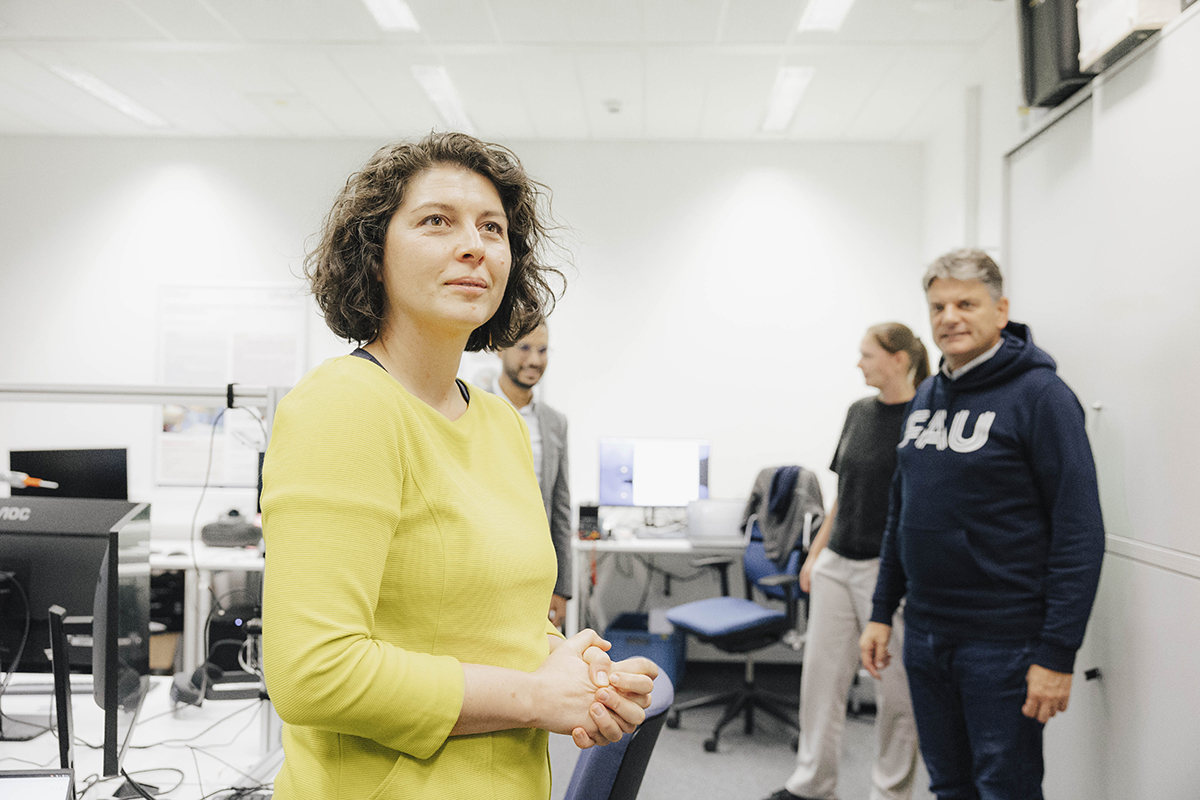 Prof. Mathis-Ullrich seht mit gefallteten Händen da und blickt nach rechts. Im Hintergrund der Präsident.