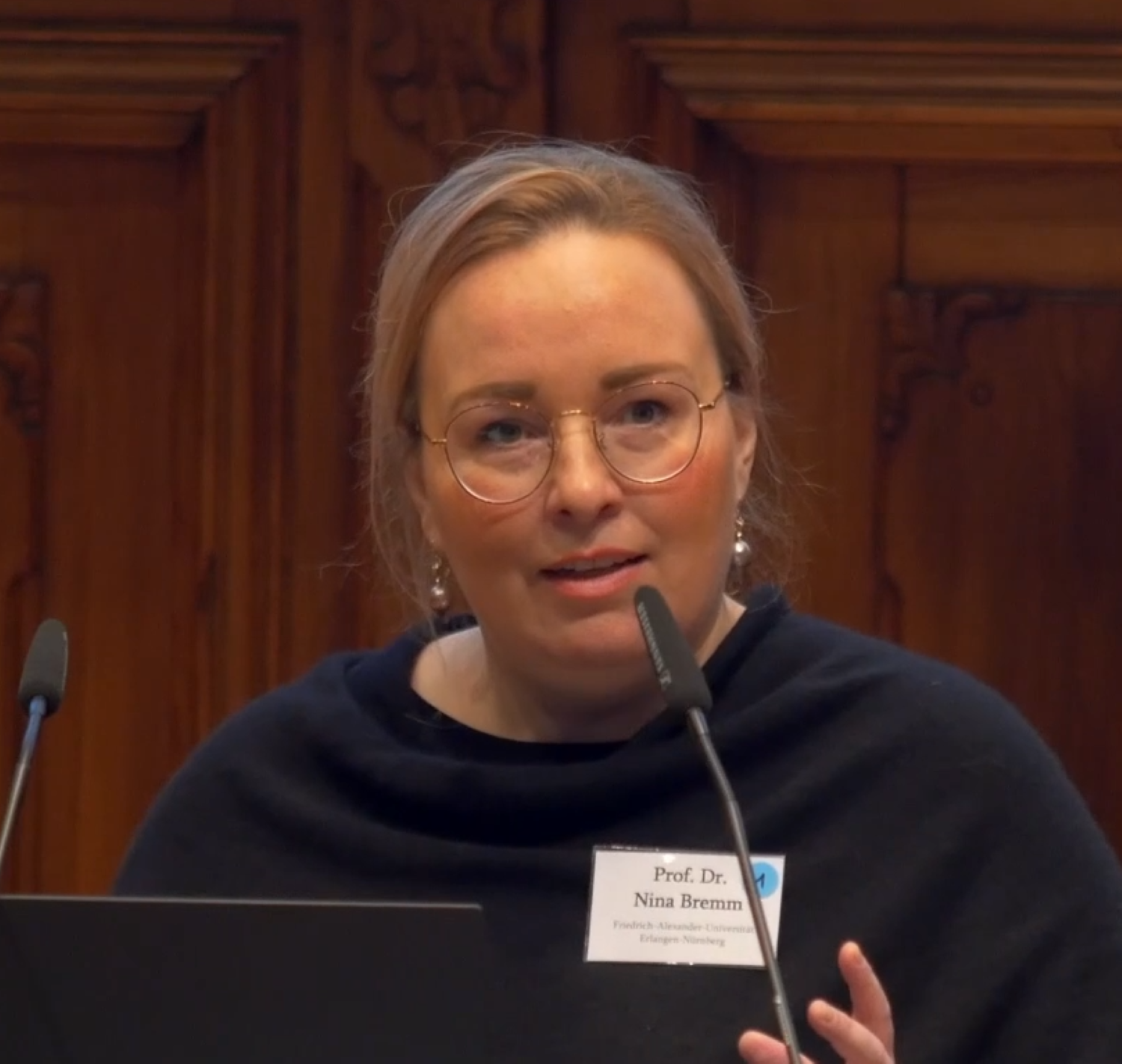 Professor Nina Bremm auf Podium an Mikrofon mit Namensschild