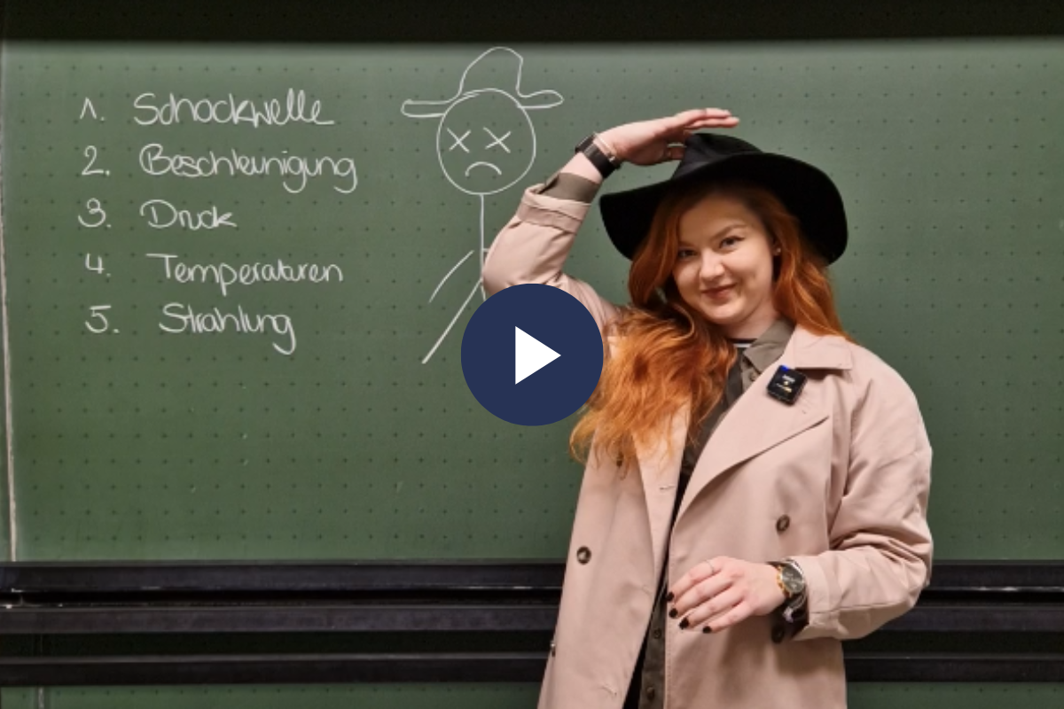 Eine Studentin, gekleidet in Trenchcoat und Schlapphut, steht vor einer Tafel. Auf dieser steht: 1. schockwelle 2. Beschleunigung 3. Druck 4. Temperaturen 5. Strahlung
