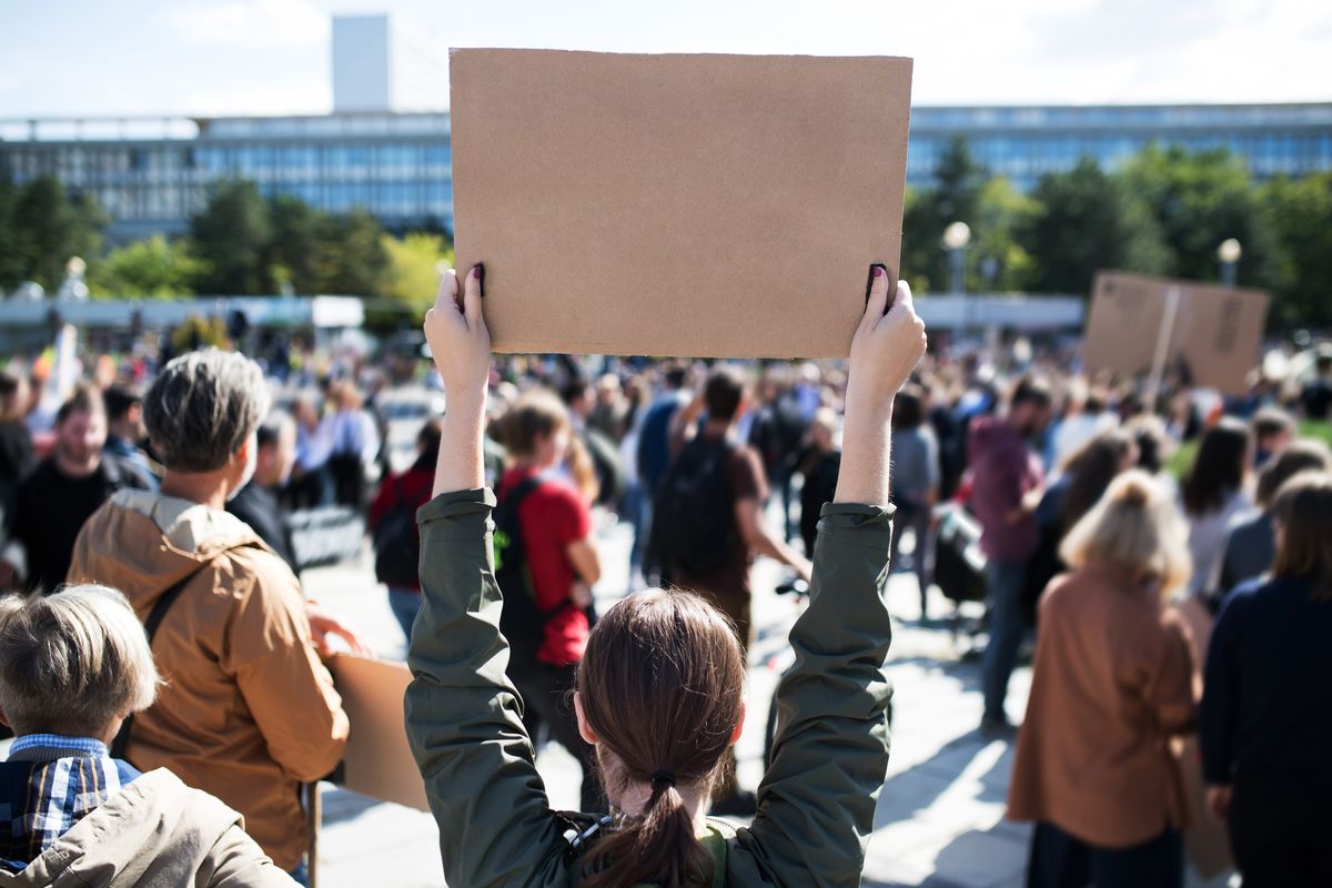 Menschen auf Demonstration, Person hält Schild hoch, von hinten kein Text zu erkennen
