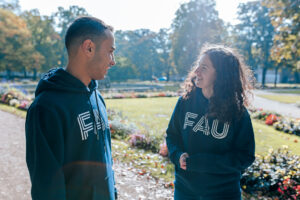Zwei junge Menschen in FAU-Pullis unterhalten sich freundlich im Schlossgarten, Erlangen