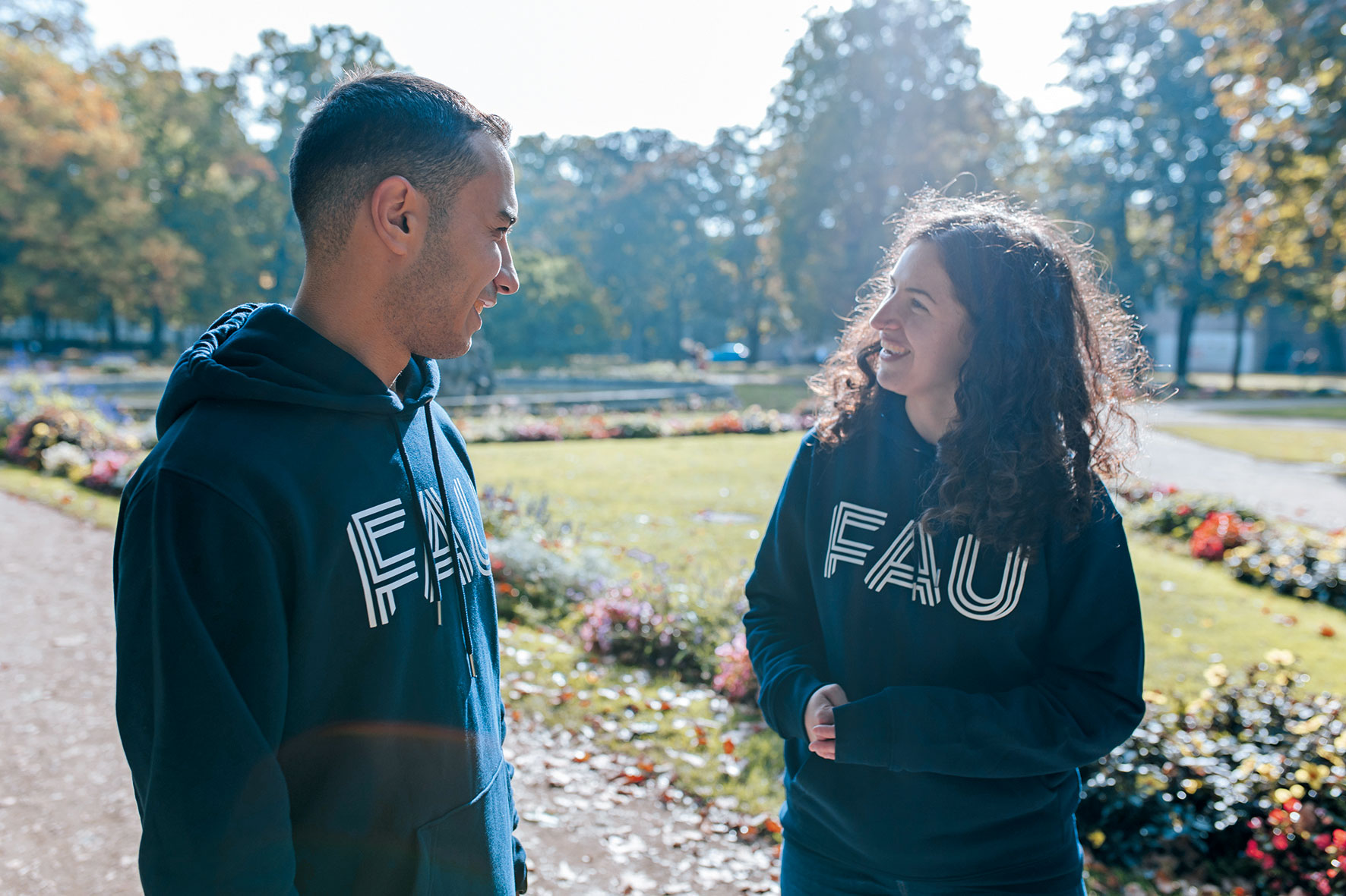 Zwei junge Menschen in FAU-Pullis unterhalten sich freundlich im Schlossgarten, Erlangen