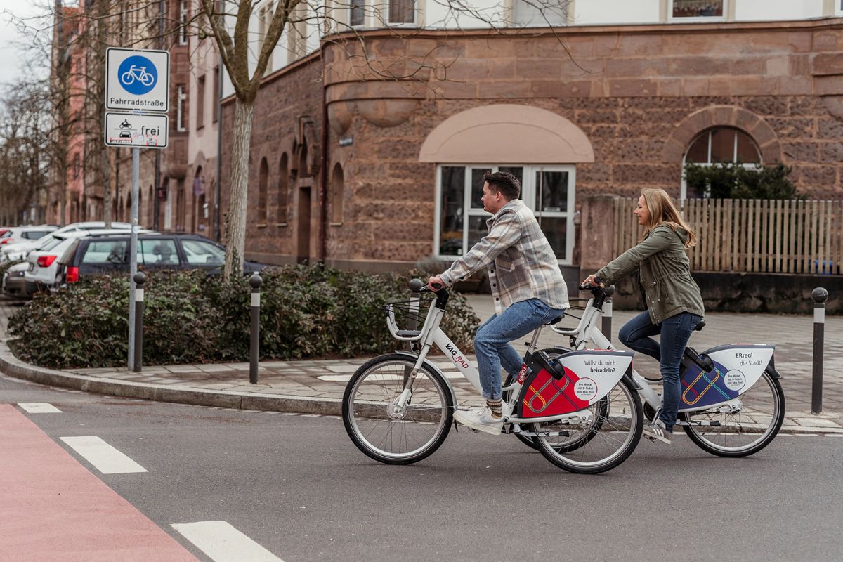 Ein Mann und eine Frau fahren auf Fahrrädern durch die Erlanger Innenstadt, die Fahrräder sind mit "VAG Rad" beschriftet