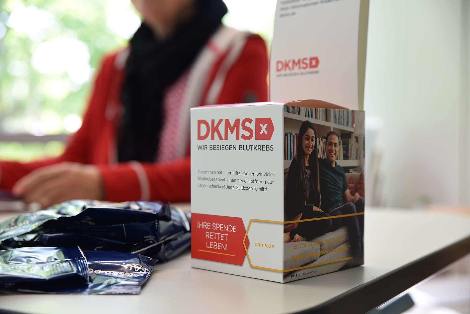 Auf einem Tisch steht ein kleiner Pappaufsteller der DKMS.