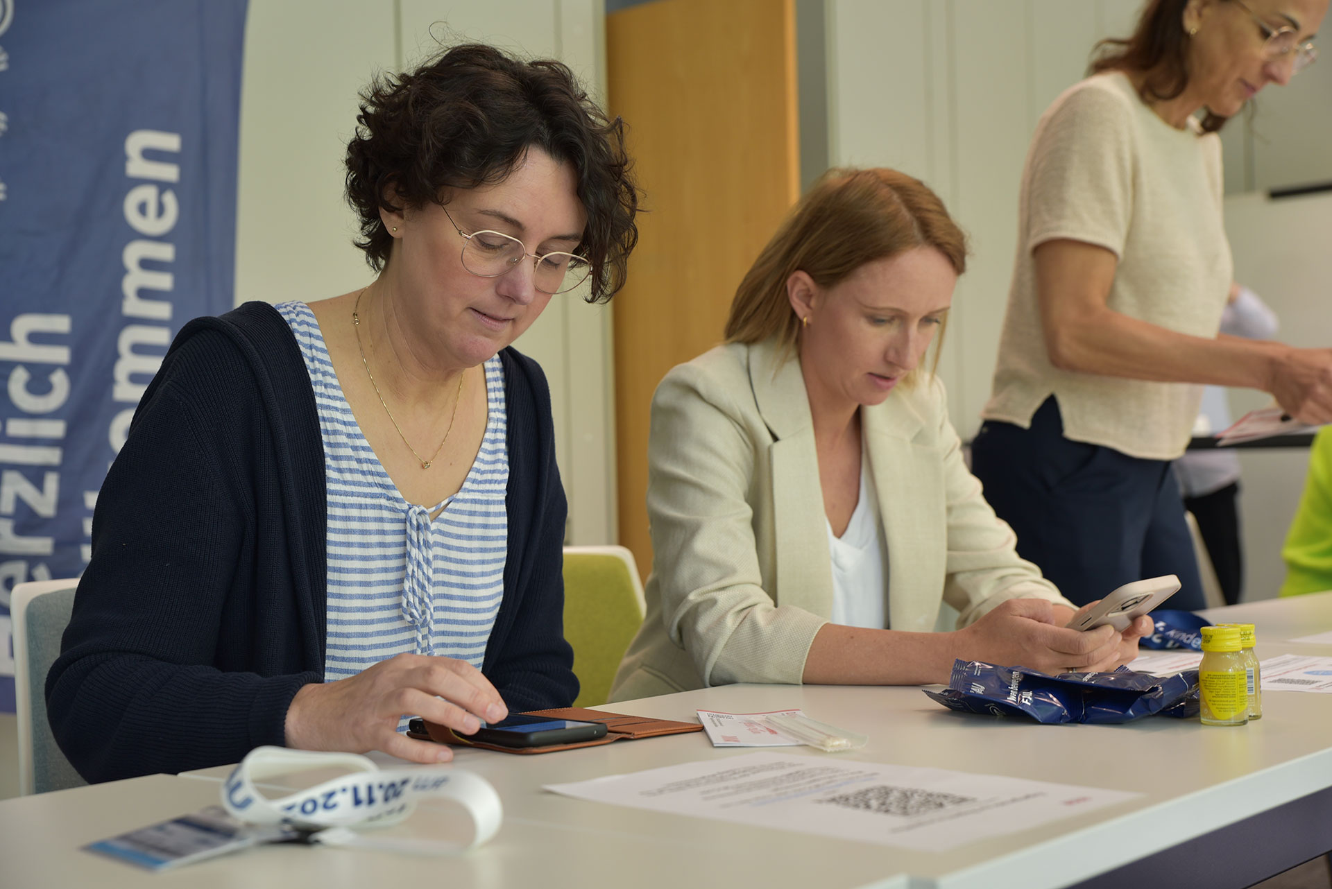 Zwei Frauen sitzen an einem Tisch und registrieren sich als DKMS-Spenderinnen am Handy.