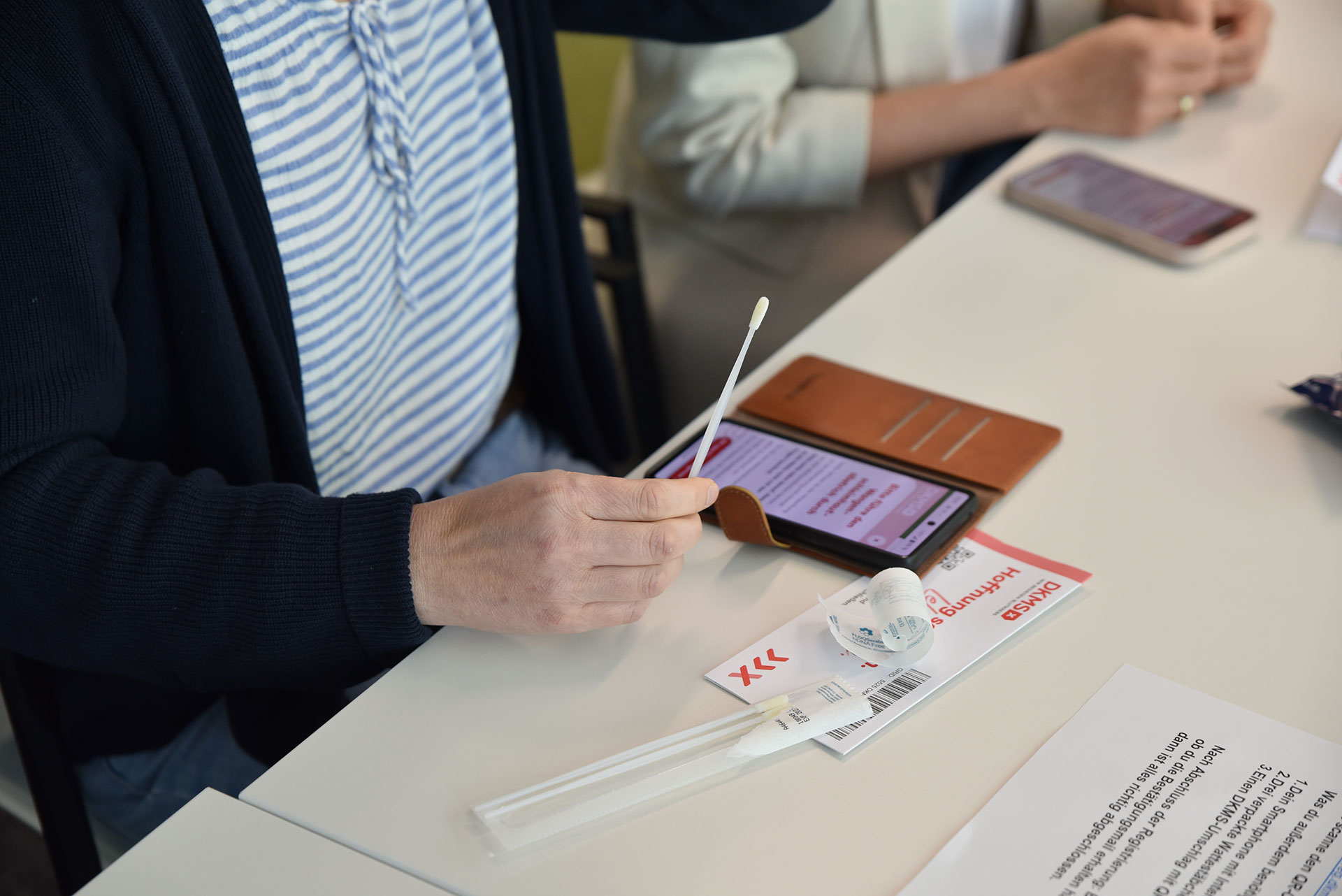 Eine Frau hält ein Wattestäbchen der DKMS in der Hand.