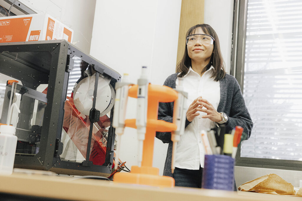 Ng vor einem Versuchsaufbau mit Schutzbrille. 