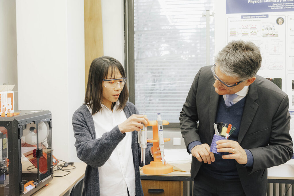 Prof. Ng erklärt Hornegger einen Aufbau. er beugt sich nach vorne um besser sehen zu können. 