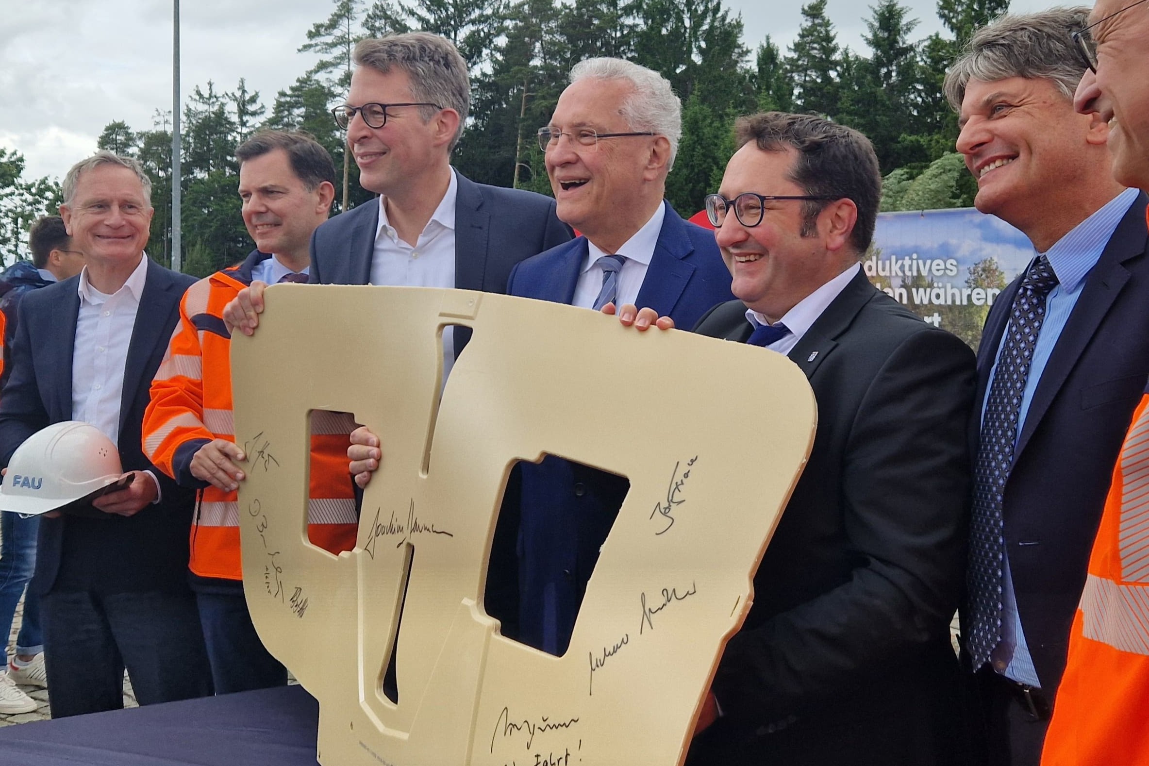 Sechs Männer in Anzügen halten einen beigen Nachbau einer Induktionsspule mit Unterschriften darauf