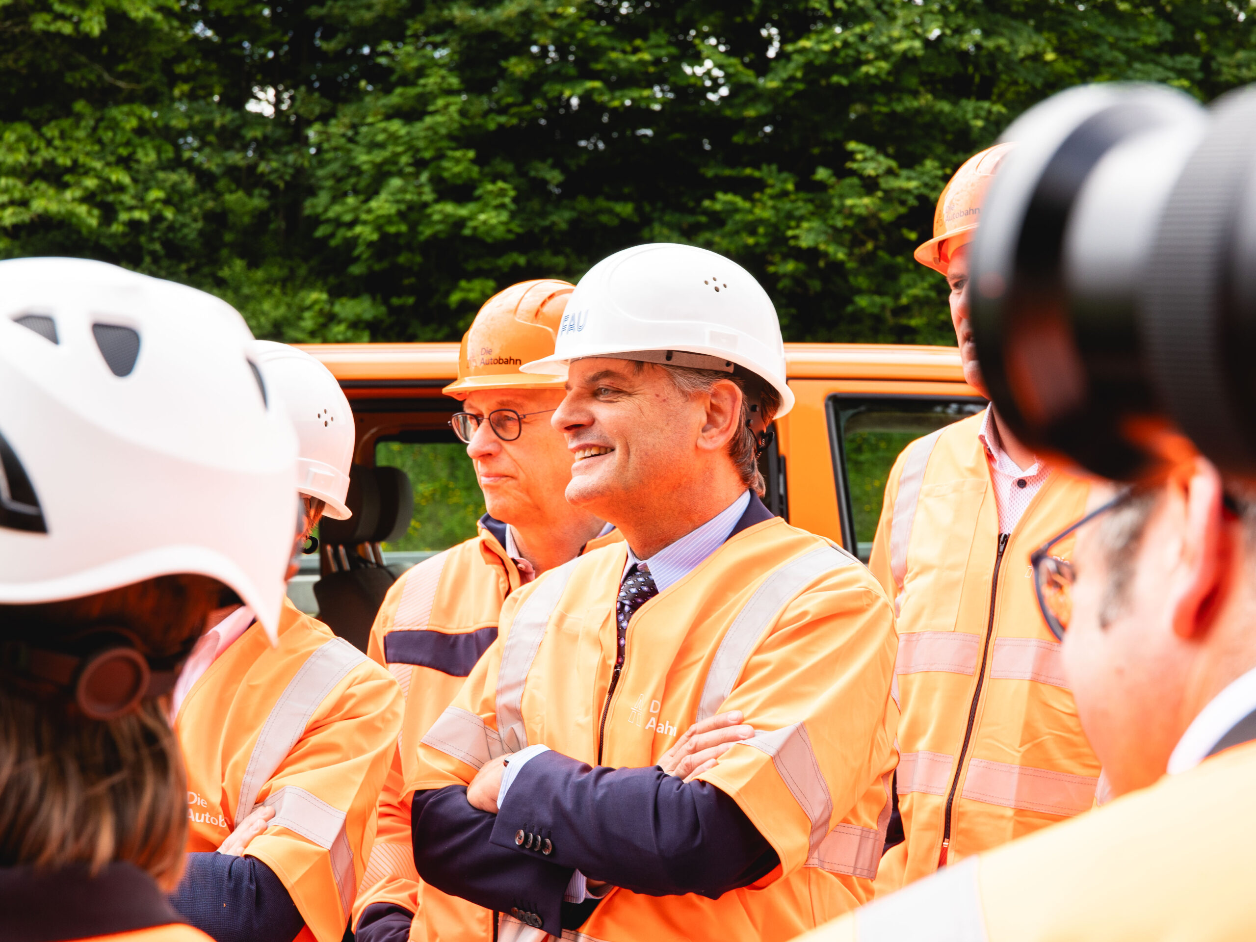 Ein Mann in Warnweste und mit Bauhelm lächelt in die Ferne.