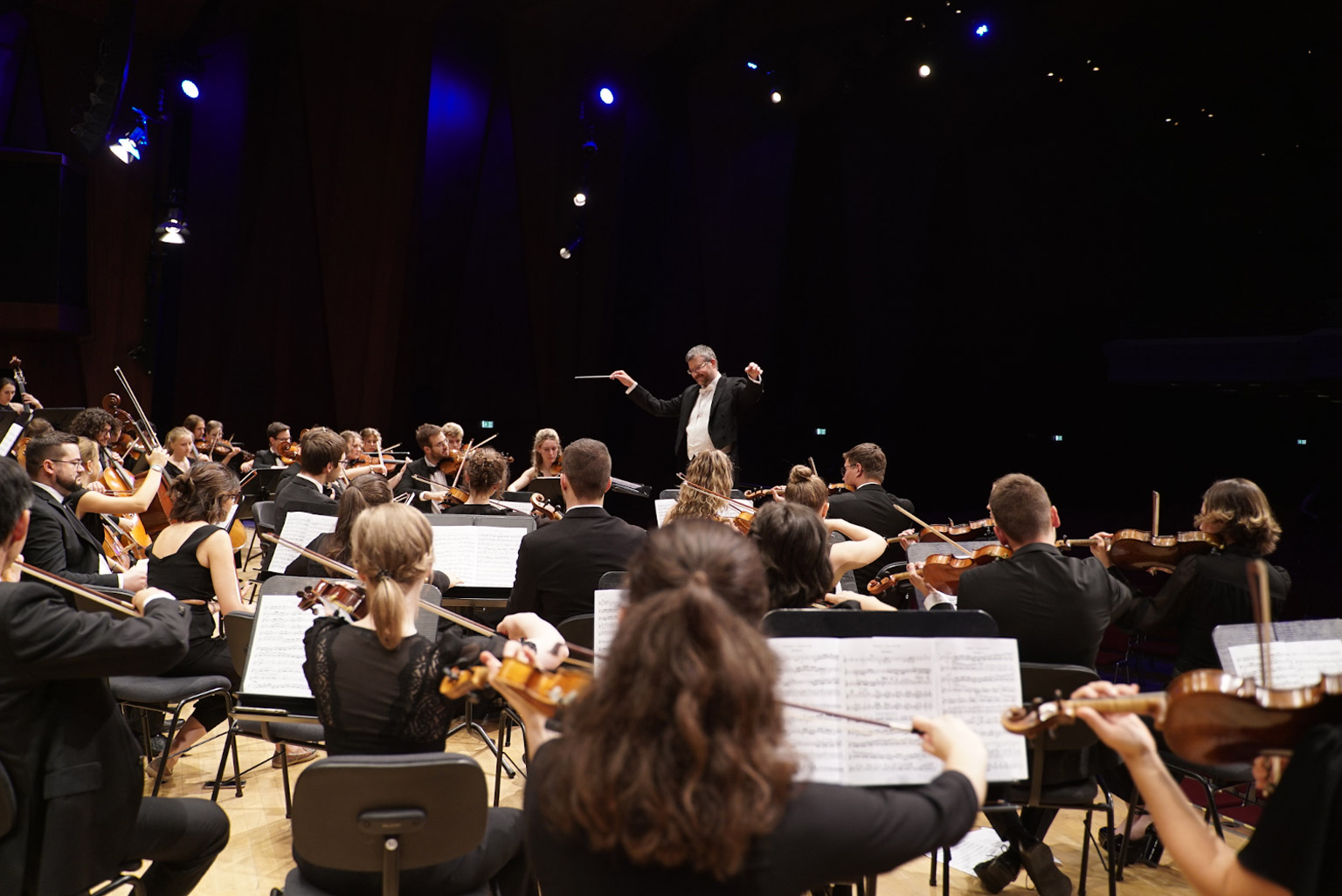 Menschen an Musikinstrumenten und Dirigent