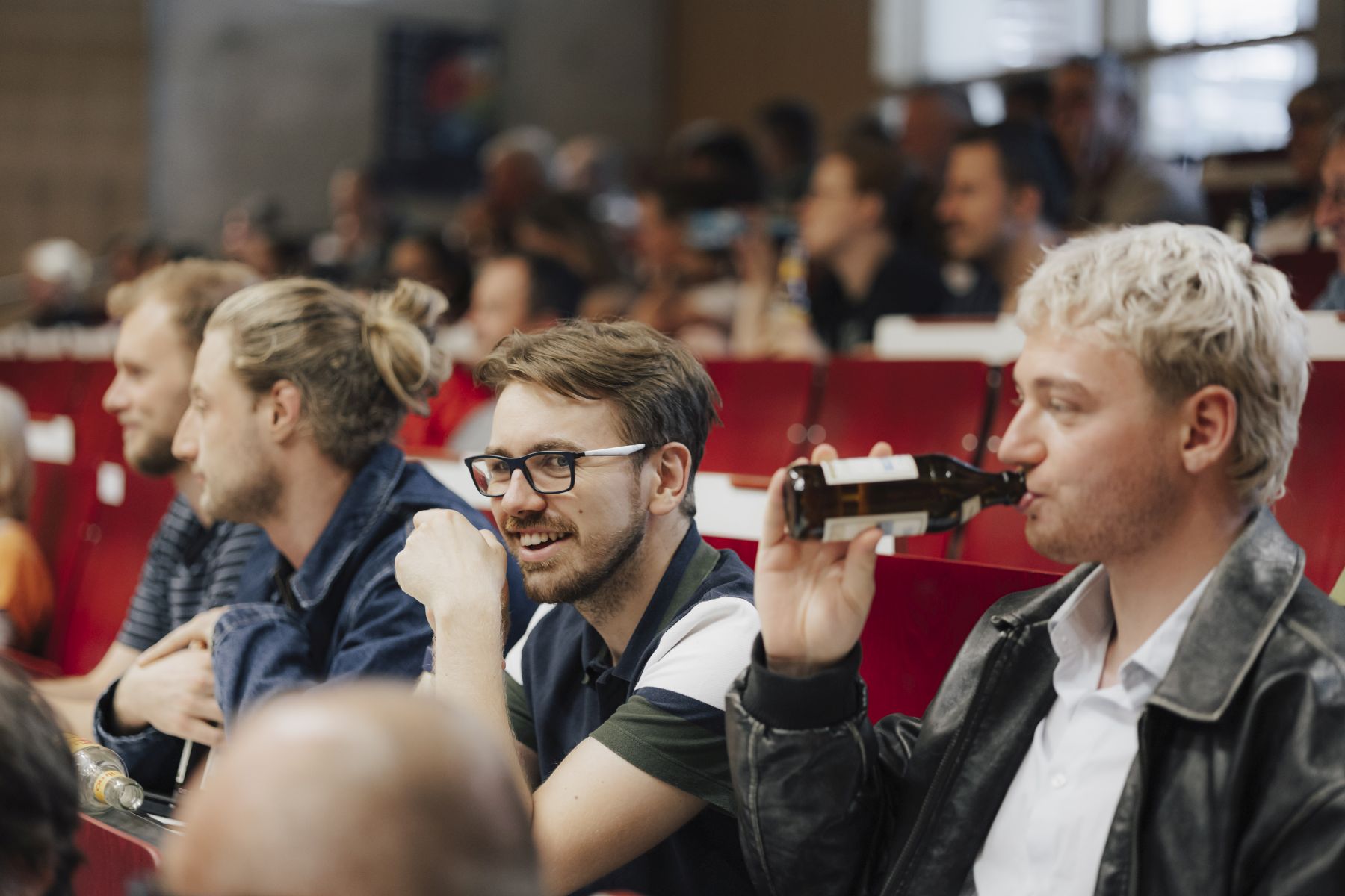 Studierende beim Scienceslam im Hörsaal, einer trinkt an Bierflasche