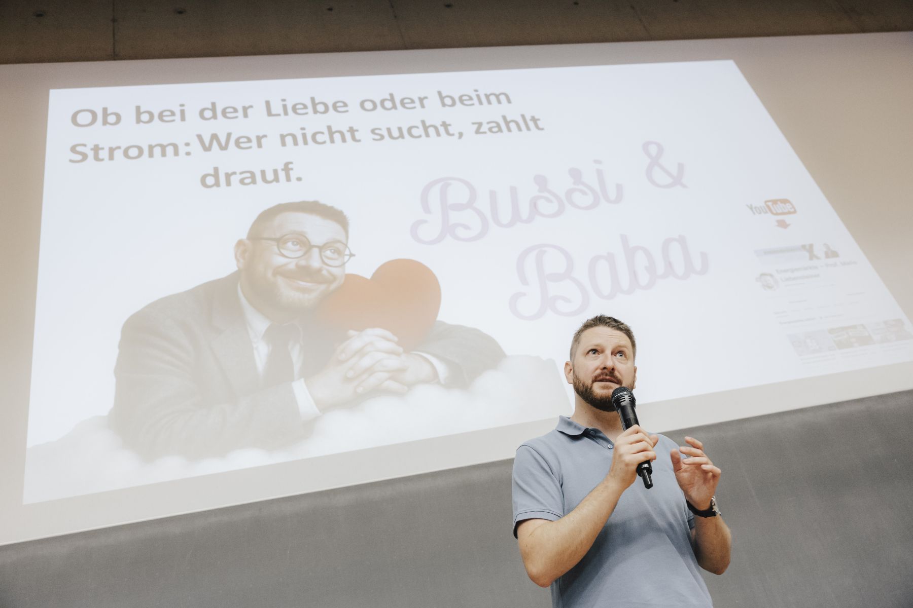 Slammer vor seiner Folie. Präsentation zeigt einen Mann im Anzug, der ein Herzkissen hält und den Text seines Slam-Vortrags 