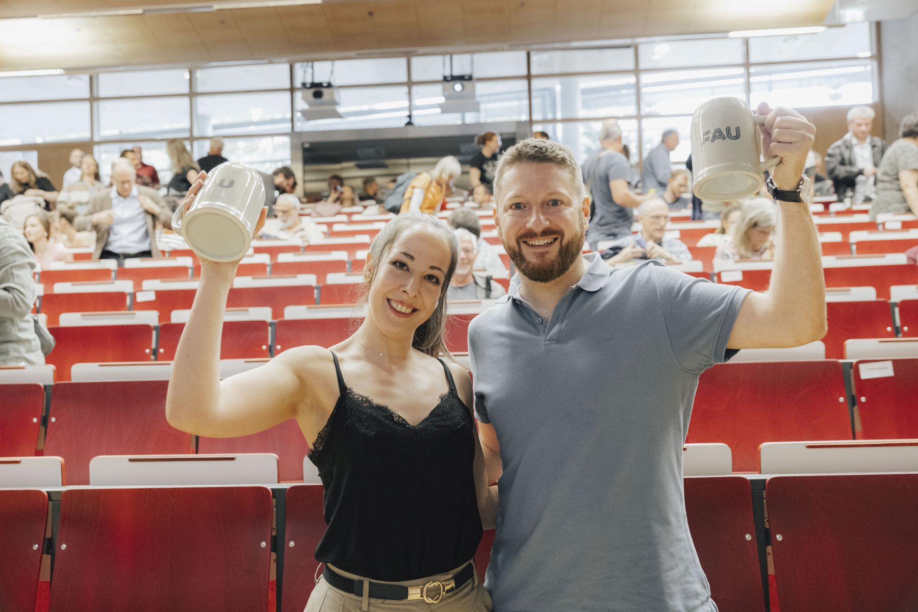 Die beiden Personen, die beim Slam aufgetreten sind mit FAU-Bierkrügen in Hörsaal