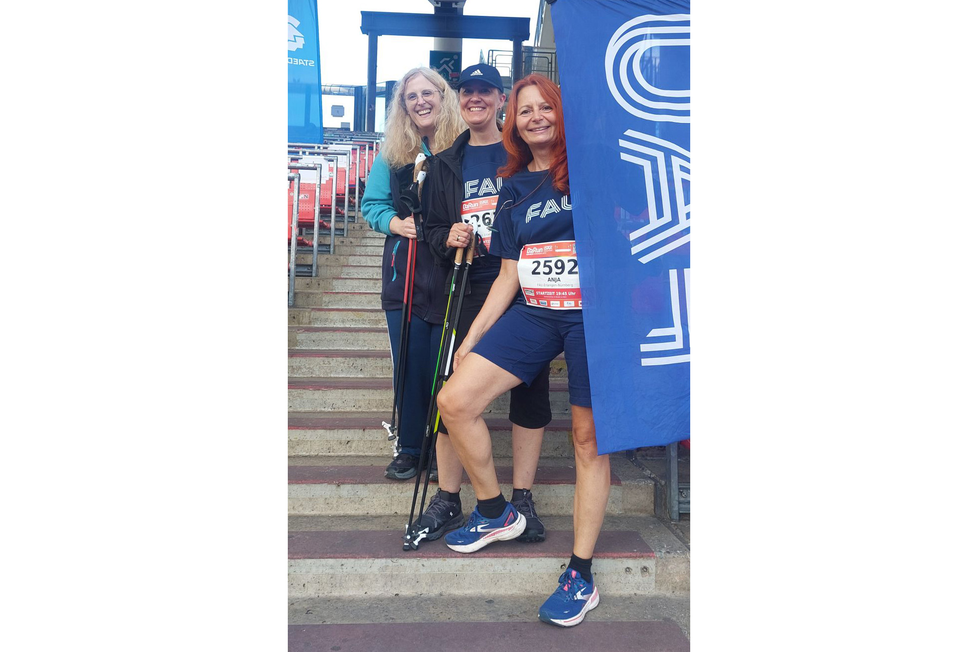 Drei Personen vor der FAU-Flagge mit FAU-Shirts