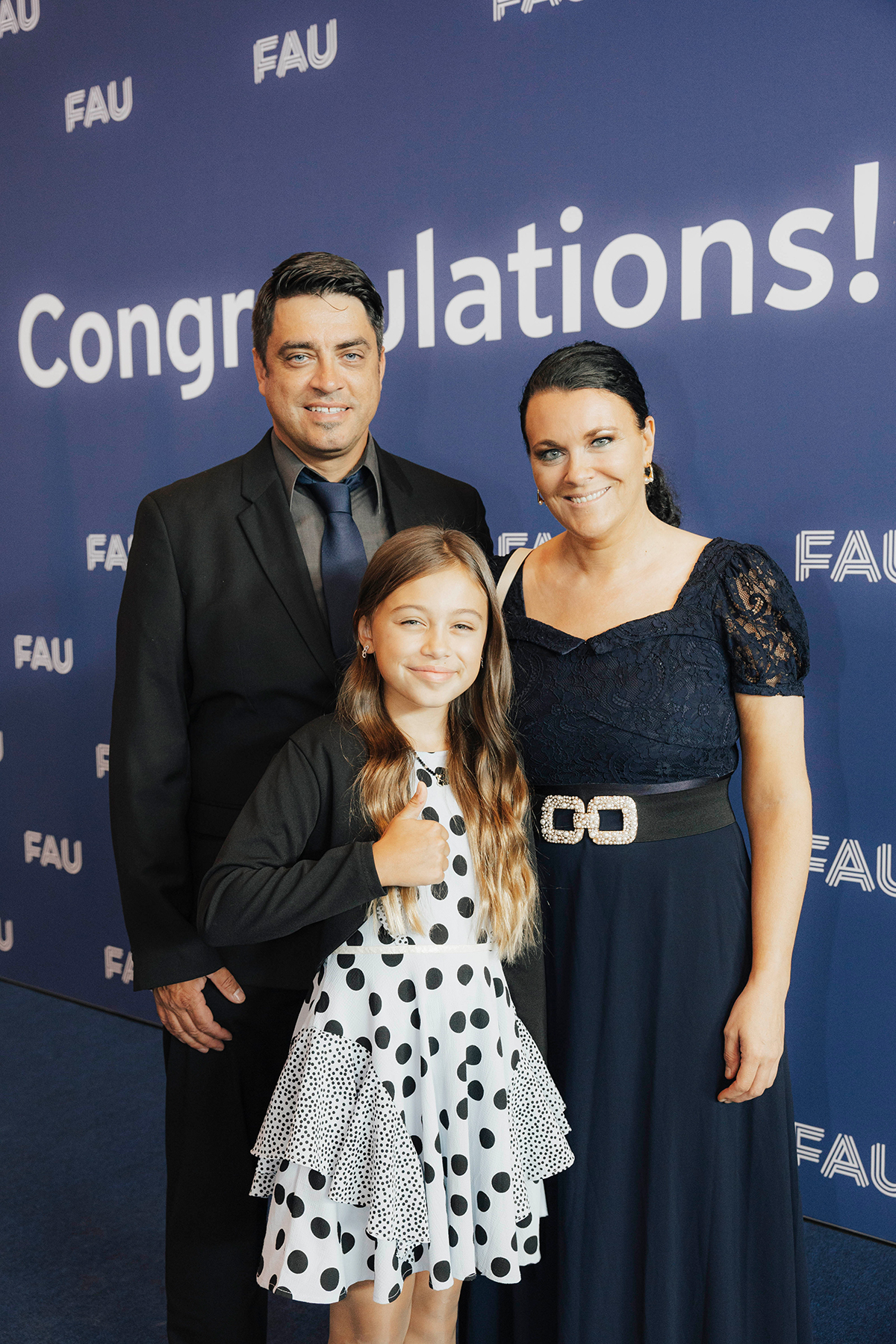 Zwei Eltern werden gemeinsam mit ihrer Tochter lächelnd vor der Fotowand abgelichtet.