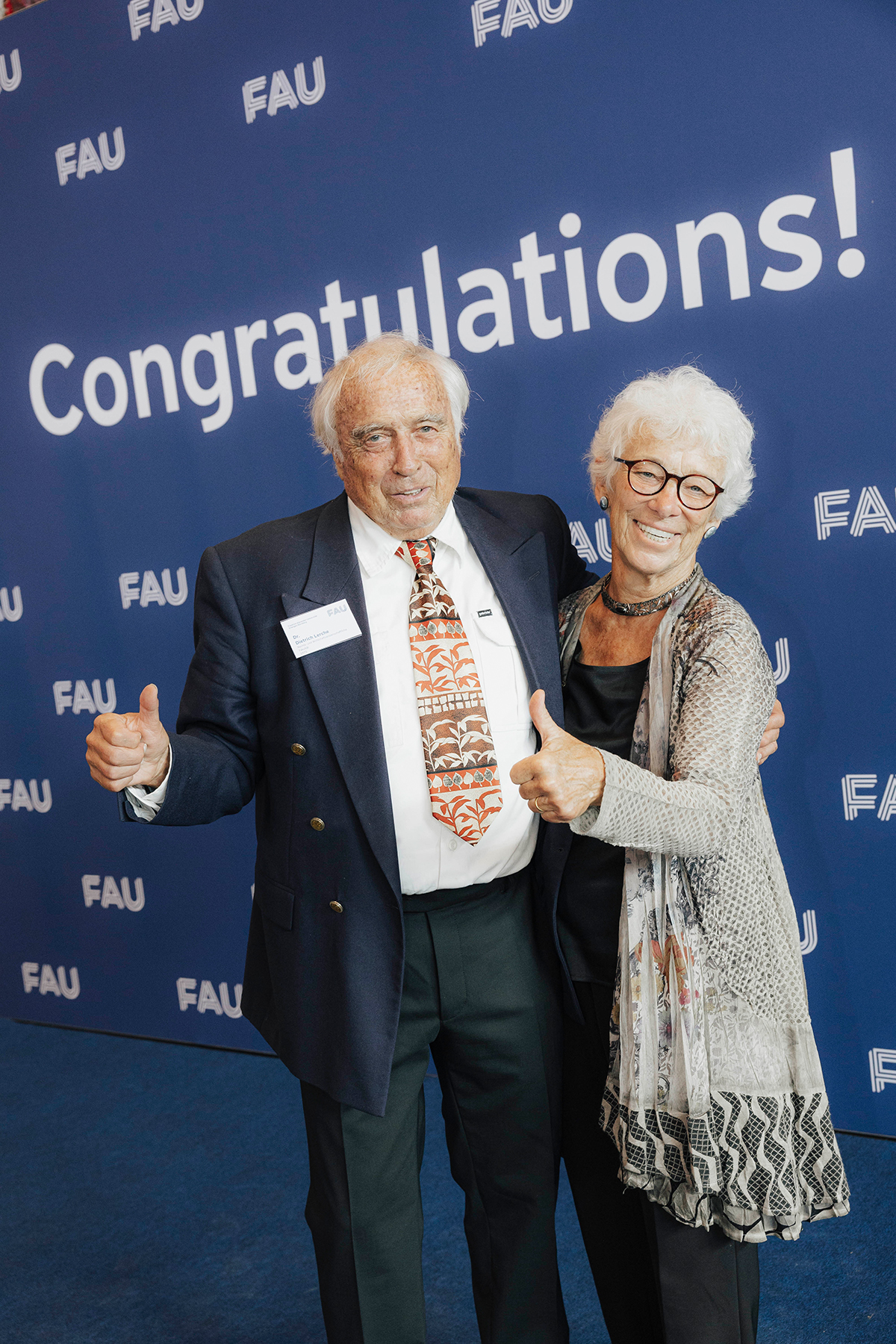 Ein lächelndes Paar wird bei der Feier vor der Gratulations-Fotowand fotografiert und gibt dabei 