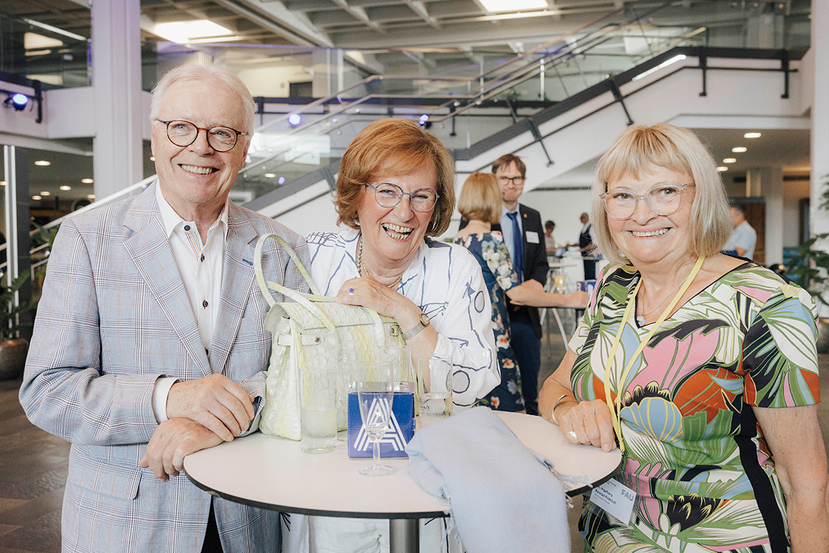 Drei Personen lächelnd an einem Stehtisch bei der Feier.