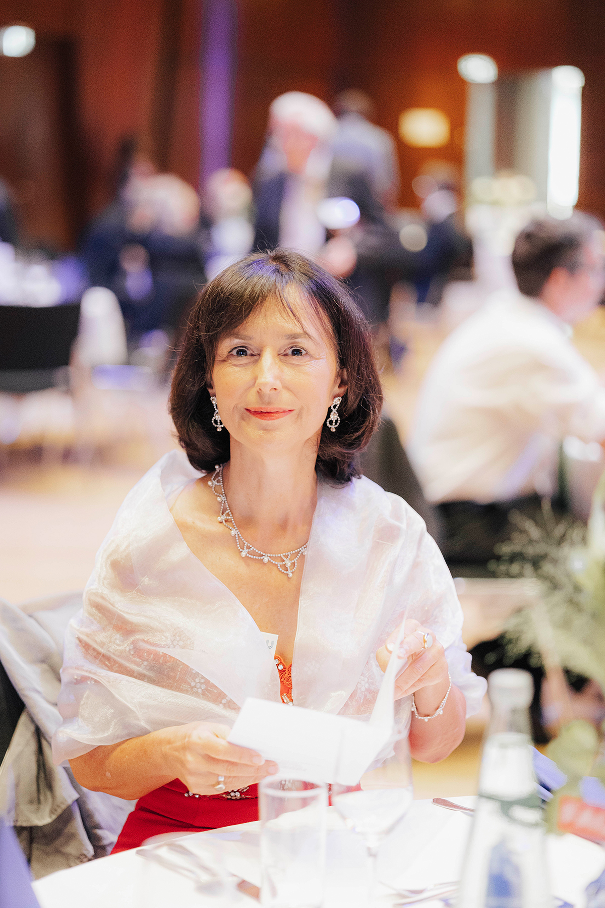 Eine Frau sitzt am Tisch und blickt leicht lächelnd in die Kamera.