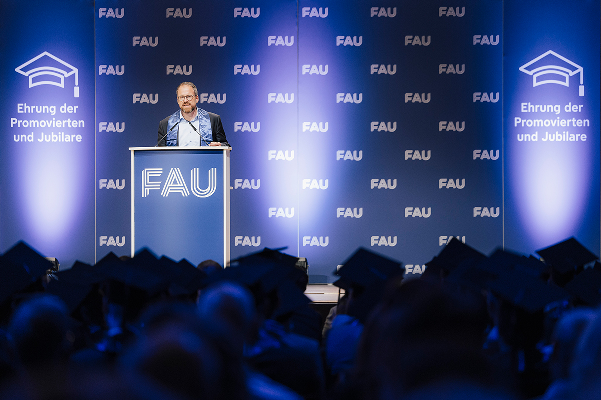 Ein Redner am Redepult auf der Bühne, Blick aus dem Publikum auf den Sprecher.