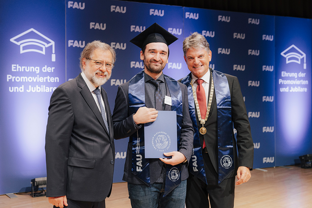 3 Männer vor der Fotowand, rechts Präsident Hornegger, mittig ein Jubilar mit Hut und Urkunde.