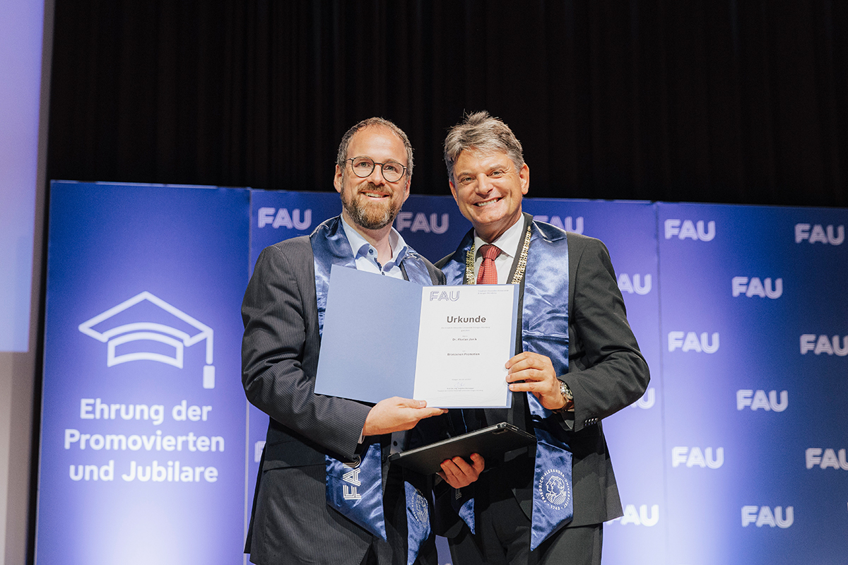 Ein Jubilar mit Urkunde und Präsident Hornegger vor der Fotowand.