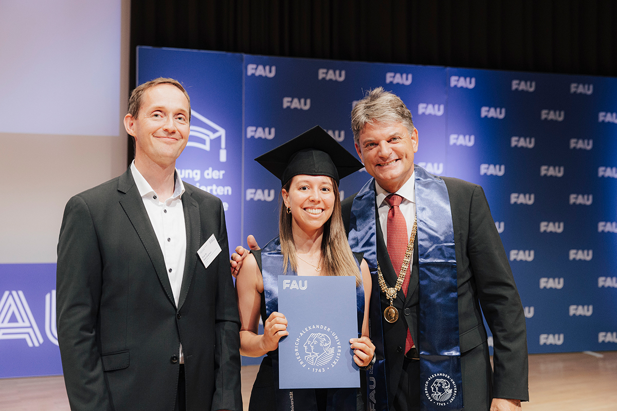 Drei Personen vor der Fotowand, in der Mitte eine Jubilarin mit ihrer Urkunde, rechts Präsident Hornegger.
