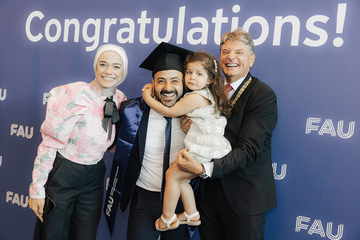 Präsident Hornegger posiert mit einem Jubilar und seiner Partnerin vor der Fotowand, seine Tochter auf dem Arm.