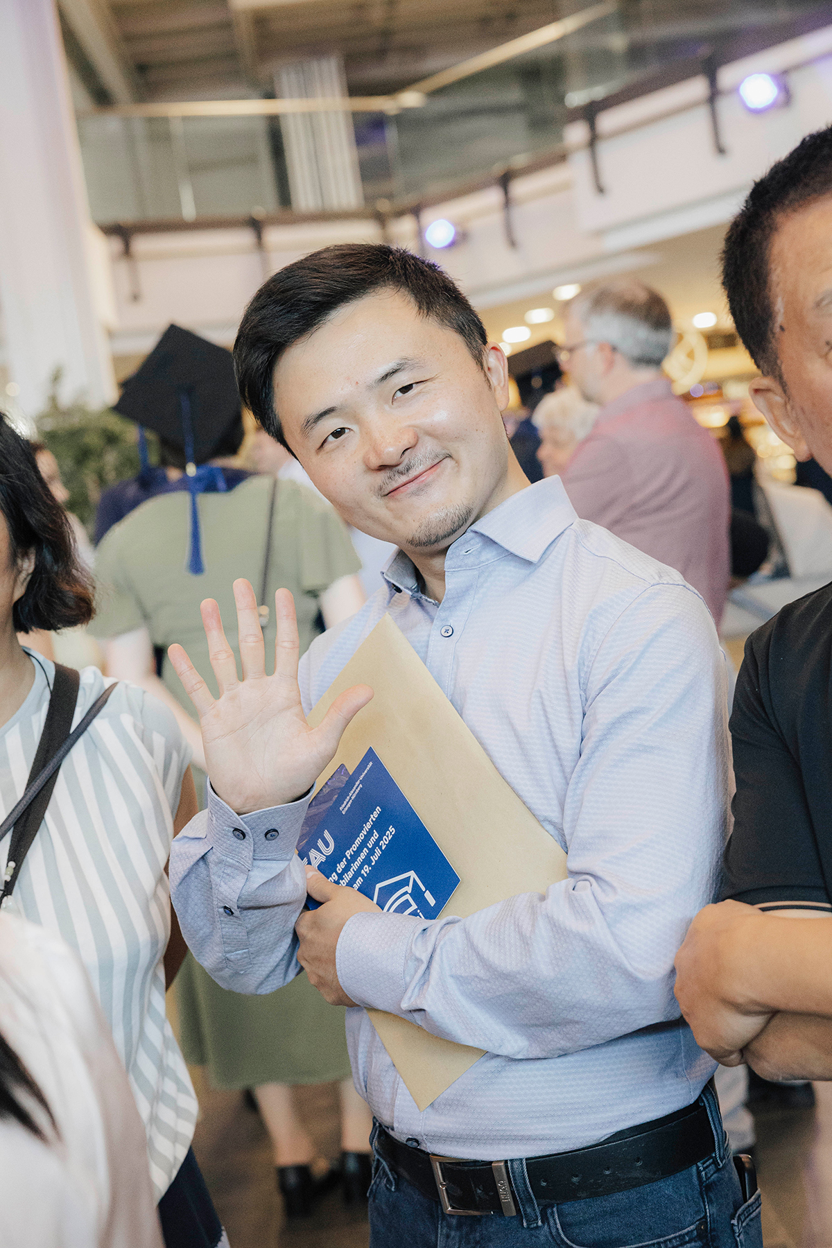 Ein Jubilar im hellblauen Hemd hebt die Hand grüßend.