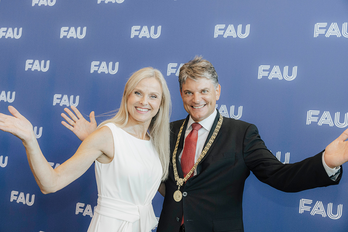 Präsident Hornegger und eine Frau strecken feierlich die Arme vor der Fotowand.