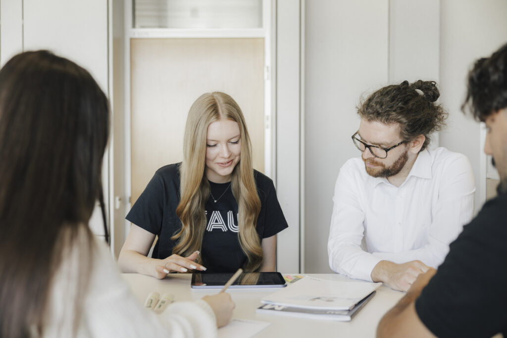 Vier Menschen sitzen gemeinsam an einem Tisch und schauen zusammen auf ein Tablet