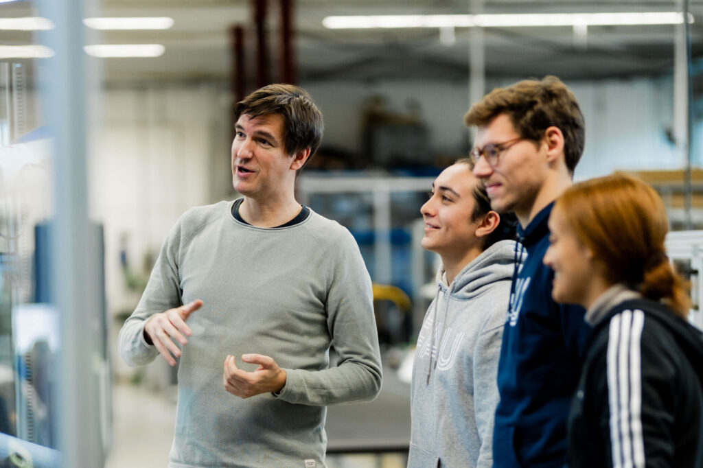 Vier FAU Forschende in einem Labor begutachten etwas an einer Maschine.