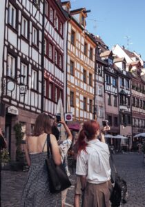 junge Menschen stehen in einer Straße und fotografieren mit ihren Handys Fachwerkhäuser