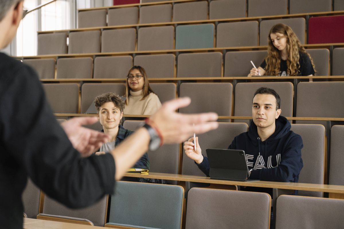 Studierende sitzen in einem Hörsaal und hören einen Dozenten zu
