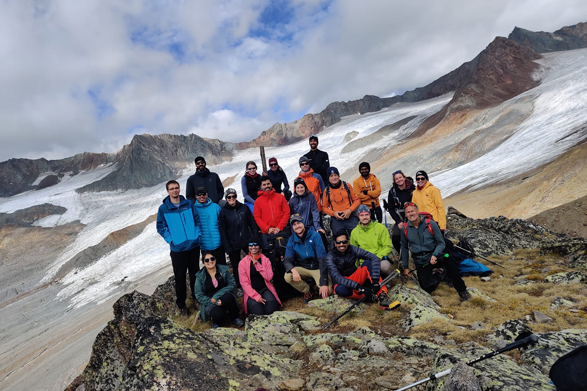 Menschengruppe auf einem Berggipfel im Hintergrund ein Gletscher.