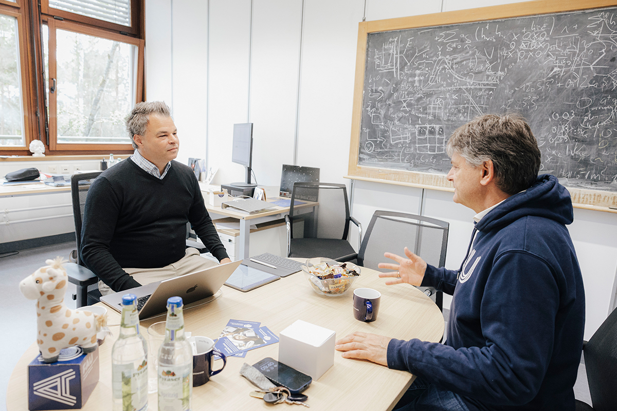 Joachim Hornegger und Kai Phillip Schmidt sitzen gemeinsam an einem Tisch und reden.