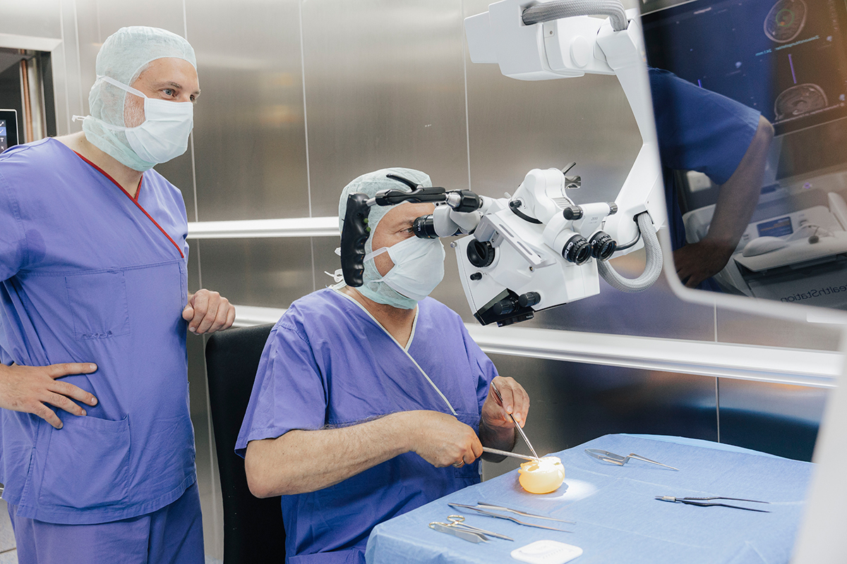 Präsident Hornegger sitzt an einem Tisch und seziert eine Paprika. Prof. Schnell steht links neben ihm und schaut ihm dabei zu.