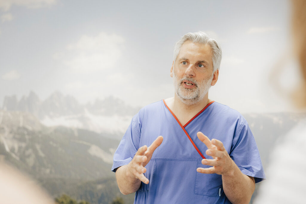 Prof. Schnell erklärt einer nicht-sichtbaren Person etwas, er hat beide Hände erhoben.