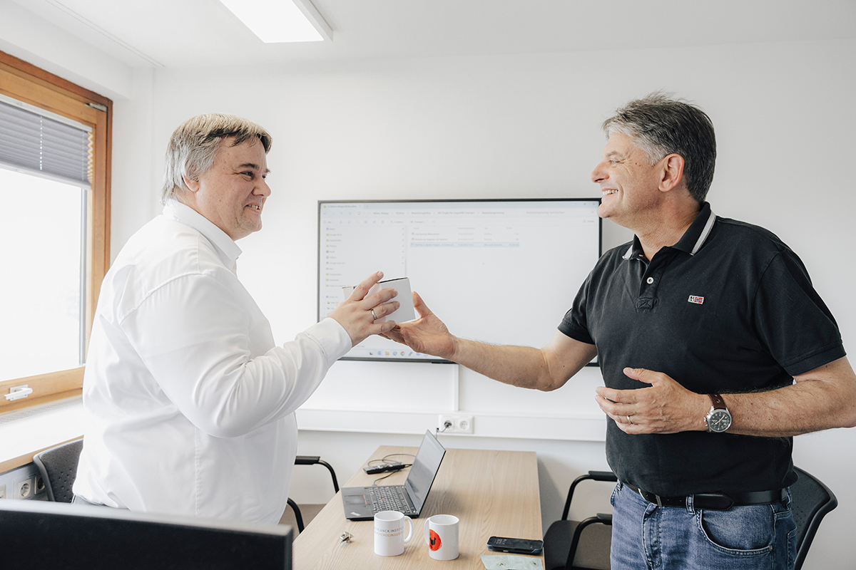 Peter Uhrig und Joachim Hornegger stehen sich gegenüber, Hornegger überreicht ein kleines Päckchen an Uhrig.