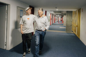 Prof. Reif und Joachim Hornegger laufen Arm in Arm durch einen Gang in der WiSo. Sie unterhalten sich dabei.